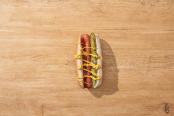 top view of delicious hot dog with pickles, mustard and ketchup on wooden table - Fotografie, Obrázek