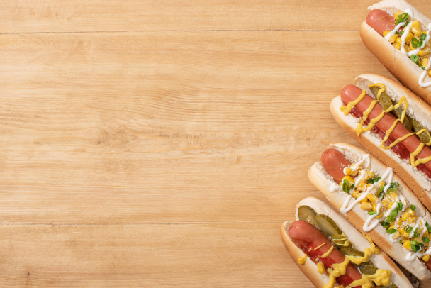 top view of delicious hot dogs with corn, green onion and pickles on wooden table - Фото, зображення