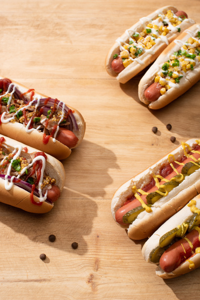delicious hot dogs with red onion, bacon, pickles and corn on wooden table - Foto, Imagem