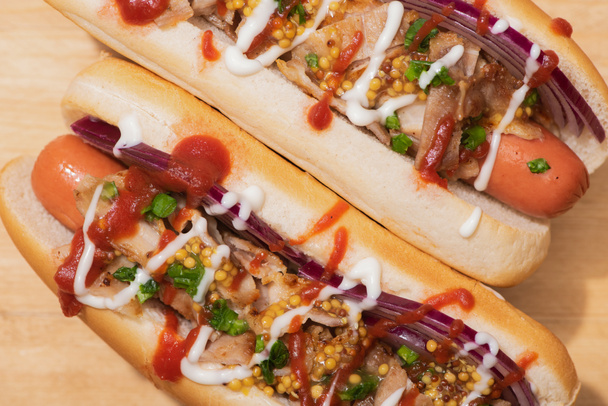 Blick von oben auf köstliche Hot Dogs mit roten Zwiebeln, Speck und Dijon-Senf auf Holztisch - Foto, Bild