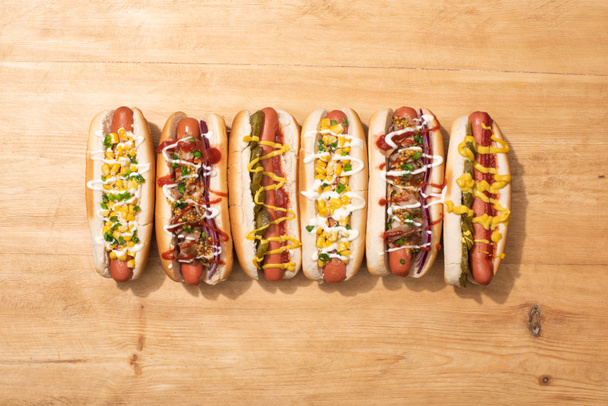 top view of various delicious hot dogs with vegetables and sauces on wooden table - Foto, Imagem