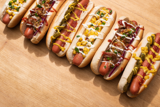 various delicious hot dogs with vegetables and sauces on wooden table - Photo, Image