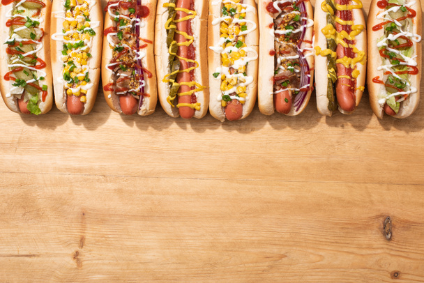 top view of various delicious hot dogs with vegetables and sauces on wooden table - Фото, зображення