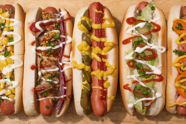 top view of various delicious hot dogs with vegetables and sauces on wooden table - Photo, Image
