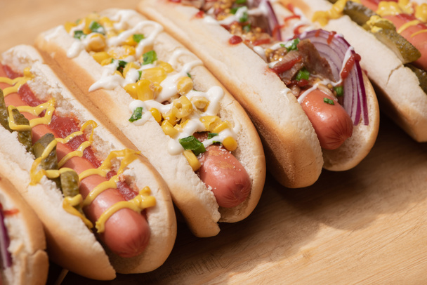 various delicious hot dogs with vegetables and sauces on wooden table - Foto, afbeelding