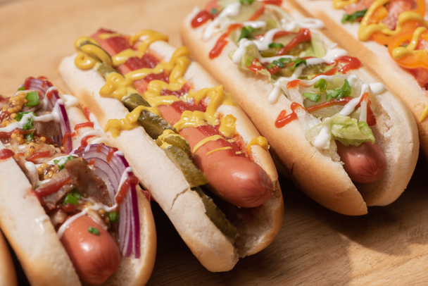 various delicious hot dogs with vegetables and sauces on wooden table - Φωτογραφία, εικόνα