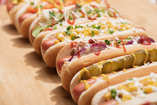 selective focus of fresh various delicious hot dogs with vegetables and sauces on wooden table - 写真・画像