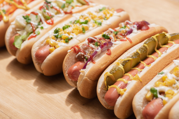 selective focus of fresh various delicious hot dogs with vegetables and sauces on wooden table - Фото, зображення