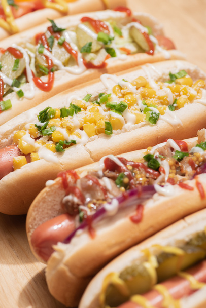 selective focus of fresh various delicious hot dogs with vegetables and sauces on wooden table - Foto, Imagem