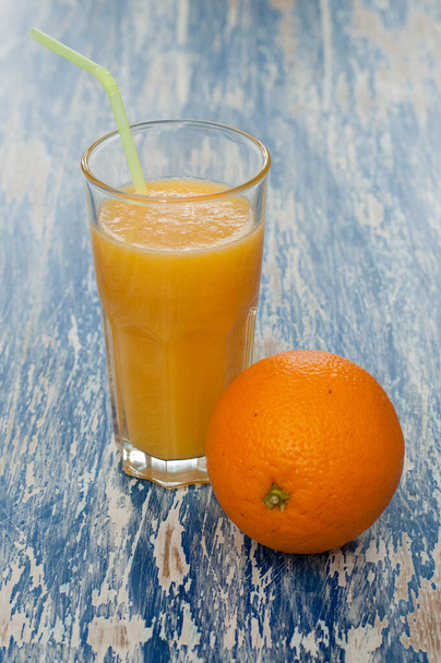 Glas Saft mit Strohhalm und Orange auf blauem Hintergrund - Foto, Bild