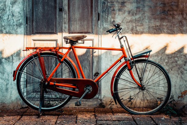 Red orange vintage bicycle parked in front of an old wall with retro wooden door with stone floor outdoor. - Fotografie, Obrázek