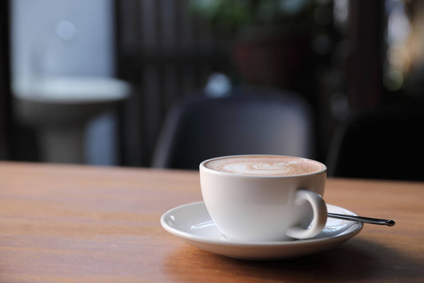 Kahve dükkanının ahşap masasındaki sütten yapılmış kapuçino ya da Latte sanat kahvesi. - Fotoğraf, Görsel