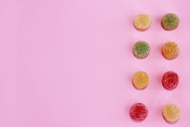 mermelada de caramelo redondo dulce multicolor en salpicaduras de azúcar sobre un fondo rosa
 - Foto, imagen