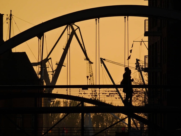Hamburg Köprüsü 'nde çift silueti ve arka planda endüstriyel temalı turuncu gün batımı. İki kişi, kopyalama alanı mevcut. - Fotoğraf, Görsel