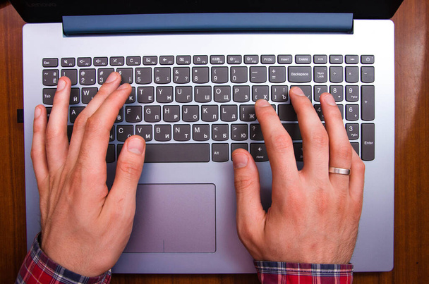 Mannen handen in een hemd in een kooi liggen op het toetsenbord op een laptop van bovenaf gezien. Handen typen op een laptop. Freelancer, programmeur. Ik typ blinden in. Werken op de laptop - Foto, afbeelding