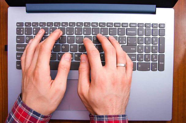 Le mani di uomini in una camicia in una gabbia si trovano sulla tastiera su un computer portatile da una vista in prima persona dall'alto. Le mani stanno scrivendo su un portatile. Libero professionista, programmatore. Digitando nel buio. Lavoro al computer portatile
 - Foto, immagini