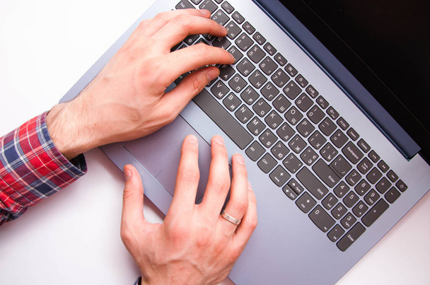As mãos masculinas em uma camisa em uma jaula estão no teclado em um computador portátil de uma visão em primeira pessoa de cima. As mãos estão a escrever num portátil. Freelancer, programador. A dactilografar cegos. Trabalho no computador portátil
 - Foto, Imagem