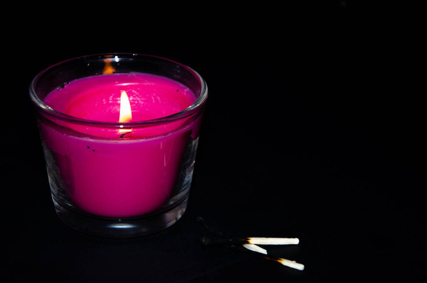 Bright pink candle in a glass jar on a black background. The candle is burning. Extinguished candle. Smoke from the candle. Hearth of fire. Tongue of flame. Macro. - Photo, Image