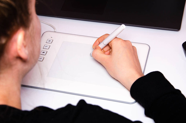 Ręce kobiet pracują na tablecie graficznym. Ręka trzyma rysik i rysuje. Biała tabliczka. Prace grafika. Dziewczyna pracuje na tablecie podłączonym do laptopa. Widok z tyłu - Zdjęcie, obraz