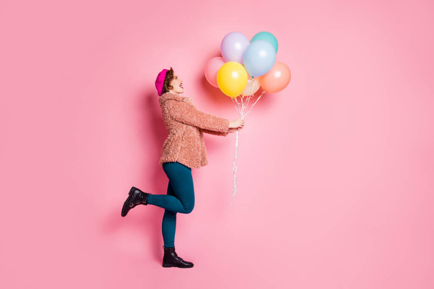 Full body profile photo of cute lady hold many colorful air balloons birthday surprise wear stylish fur coat scarf beret cap pants shoes clothes isolated pink color background - Foto, imagen