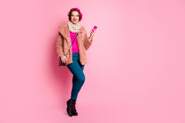 Full length photo of cute traveler lady hold telephone walk down street making pictures wear casual spring fur coat beret pants shoes clutch outfit isolated pink color background - 写真・画像