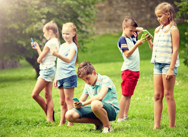 niños con smartphones jugando en el parque de verano
 - Foto, Imagen