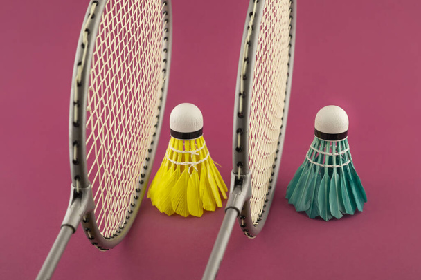 Badminton raketleri ve punk arka planında mavi ve sarı tüylü mekikli horozlar. - Fotoğraf, Görsel
