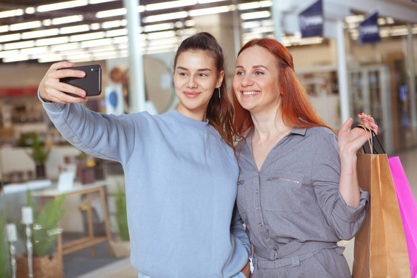Nuori kaunis nainen ottaa selfie ystävänsä kanssa ostoksilla ostoskeskuksessa yhdessä
 - Valokuva, kuva