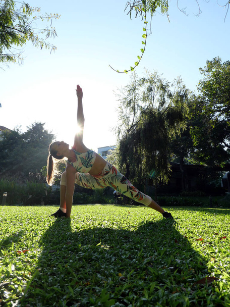 Mujer joven práctica extendido lados ángulo yoga pose en verde hierba exterior. Foto vertical
. - Foto, imagen