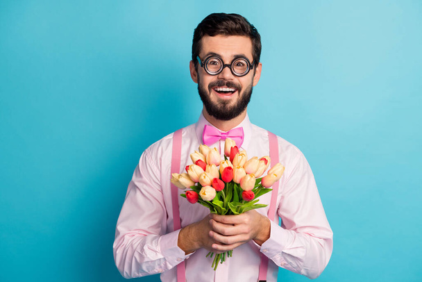 Verrückte positive Geek Kerl High School Student fühlen sich aufgeregt über 14-Februar Feier Datum mit Schönheitskönigin Mädchen geben ihr Tulpen Geschenk tragen rosa Hemd isoliert blaue Farbe Hintergrund - Foto, Bild