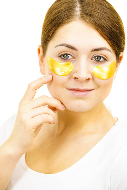 Young woman applying golden collagen patches under eyes. Mask removing wrinkles and dark circles. Girl taking care of delicate skin around eye. Beauty treatment. - Foto, immagini