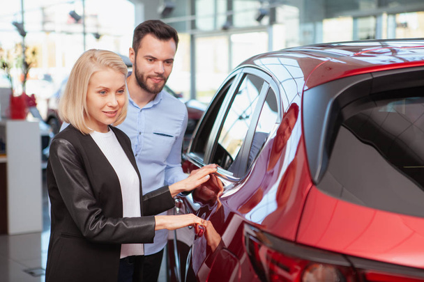 Happy couple examining new automobile at car dealership, copy space. Beautiful woman and her husband choosing new auto to buy - Foto, immagini