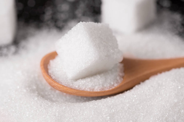 Sugar sand and sugar cubes poured from a wooden spoon. - Photo, Image