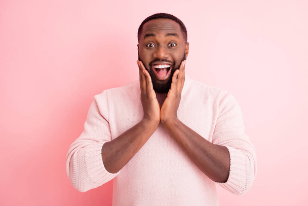 Photo of funny attractive dark skin young guy toothy beaming smiling listen good news open mouth arms on cheekbones wear warm knitted sweater isolated pink color background - Foto, afbeelding