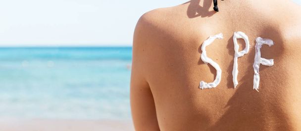Jeune fille a spf mot sur le dos fait de crème solaire à la plage. Concept de facteur de protection solaire
. - Photo, image