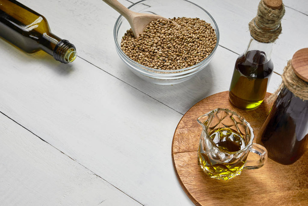 Hemp seed in glass bowl on the table, Cold pressed oil in a glass jar and bottle on the background of wooden boards - Fotografie, Obrázek