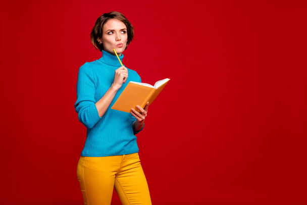 Portrait of clever concentrated girl prepare for lecture make project think thoughts hold copy book touch pencil cheek look copyspace wear blue yellow jumper isolated red color background - Zdjęcie, obraz