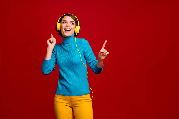 Portrait of charming cheerful girl listen music with stylish ear phones sing song dance like dj wear trendy look copy space outfit isolated over red color background - Photo, Image
