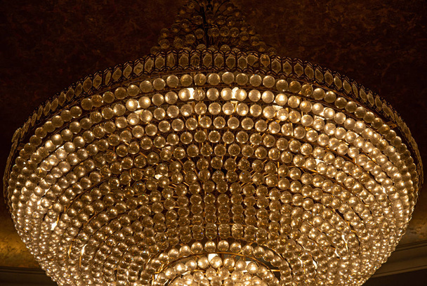 Chandelier in temple. Luxury shiny texture of circle rows of diamond shaped glass gems closeup. Glamour shiny backdrop with copy space. Close-up of gorgeous chandelier with crystal pendants. - Photo, Image
