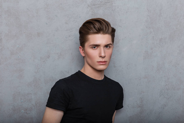 Studioporträt eines modischen jungen Mannes mit sauberer Haut mit durchbohrter Nase und trendiger Frisur in einem stylischen schwarzen T-Shirt auf grauem Hintergrund im Zimmer. - Foto, Bild