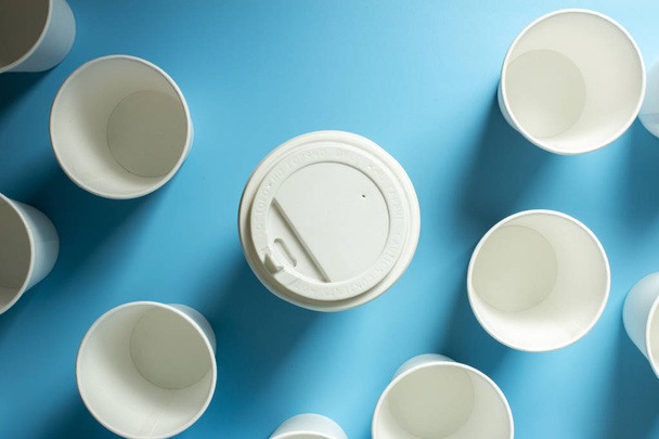 One cup of coffee is surrounded by empty Paper cups for drinks on a blue background. Concept friendly team, leader, director, boss. Banner. Flat lay, top view. - Foto, Bild