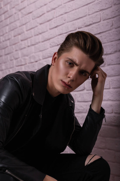 Closeup studio portrait of a young cool man with clean skin with nose piercings in a vintage black leather jacket near pink brick wall. Handsome stylish sexy guy hipster with fashion hairstyle indoors - Foto, Imagem