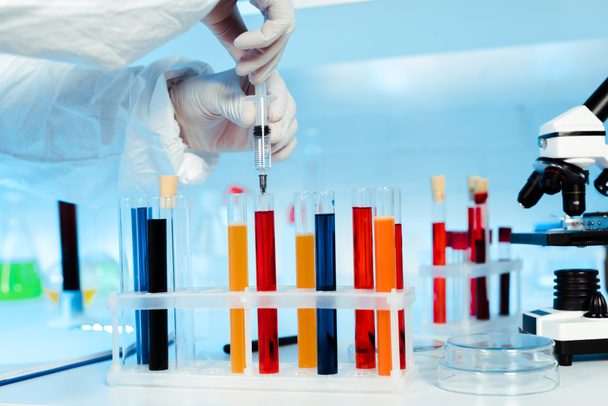 cropped view of scientist holding syringe near test tubes with samples  - Foto, Bild