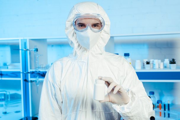 scientist in hazmat suit and goggles holding bottle in laboratory  - Photo, Image