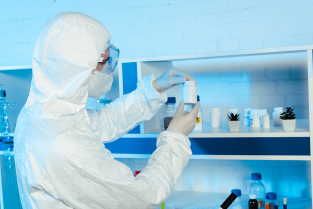 científico en guantes de látex y gafas mirando botella en laboratorio
  - Foto, Imagen