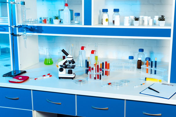 kolven, reageerbuizen en flessen in de buurt van microscoop in modern laboratorium  - Foto, afbeelding