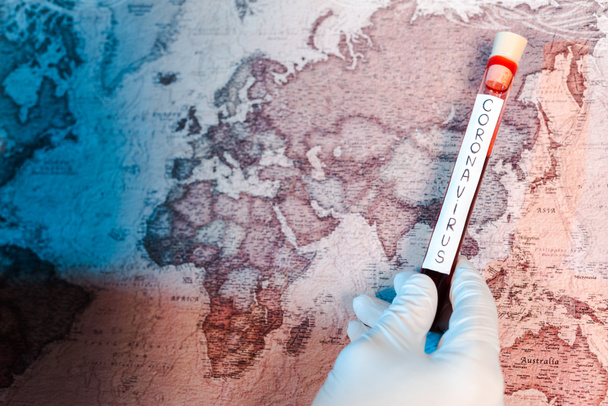 cropped view of scientist holding test tube with coronavirus lettering near map  - Foto, afbeelding