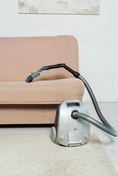 vacuum cleaner on carpet near modern sofa in living room  - Фото, изображение
