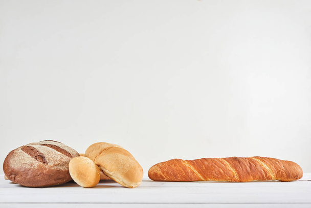 Assortment of baked bread and baguette on a white wooden table. Copy space and wide background - Foto, Imagen
