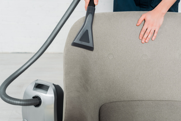 cropped view of young cleaner dry cleaning armchair with vacuum in modern living room  - Valokuva, kuva